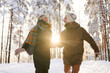 © Seventyfour - Portrait of playful couple running towards camera in winter forest and smiling happily lit by  sunlight, copy space