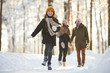 © Seventyfour - Full length portrait of happy little girl running towards camera in winter forest while enjoying walk with family, copy space