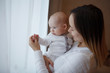 © olgasparrow - Young happy loving mother plays with a baby on her hands against the window. Maternal care. Childcare. Close-up.