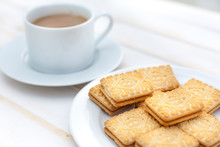 Several Custard Cream Biscuits On A White Plate With A Cup Of Coffee In The Background On A White Table.