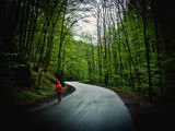 Fototapeta Dziecięca - Człowiek w kapturze idący w deszczu przez las asfaltową drogą
