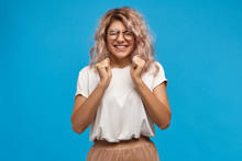 Success, Positive News, Joy And Happiness Concept. Ecstatic Excited Adorable Stylish Girl In Trendy Round Glasses Smiling Broadly And Clenching Fists, Glad To Receive Present On Her Birthday