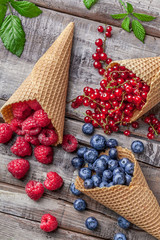 Wall Mural - Forest fruit berries in ice cream cones with green leaves on wooden table overhead arrangement studio shot