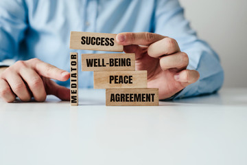 Wall Mural - The role of the mediator in maintaining stability in life. Man arranges wooden blocks with inscription PEACE, AGREEMENT supported by a wooden MEDIATOR block. Role of mediation in maintaining order.