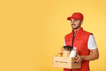 Sticker - Food delivery courier holding wooden crate with products on color background. Space for text