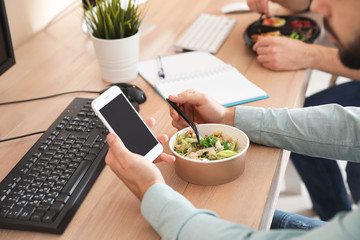 Canvas Print - Office employee with smartphone having lunch at workplace, closeup. Food delivery