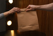 © New Africa - Man giving paper bag with order to customer in cafe, closeup. Mock up for design