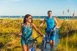 © Maridav - Summer people lifestyle happy couple biking on beach relaxing outdoors activity at sunset. Young woman and man riding leisure bicycles on USA Florida holidays getaway.