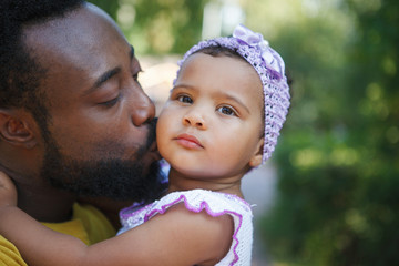 African father holds his little daughter in his arms, hugs and kisses.