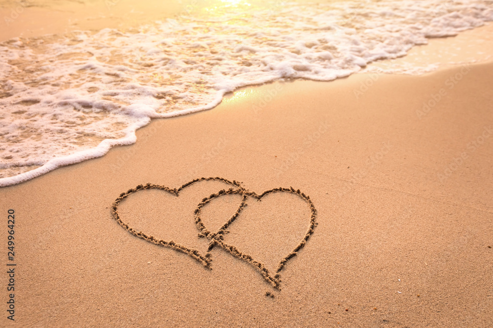 Romantic honeymoon holiday or Valentine's day on the beach concept with two hearts drawn on the sand, tropical getaway for couples, love symbol