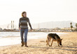 Happy attractive young woman with her german shepard dog walking on the beach at autumn sunset