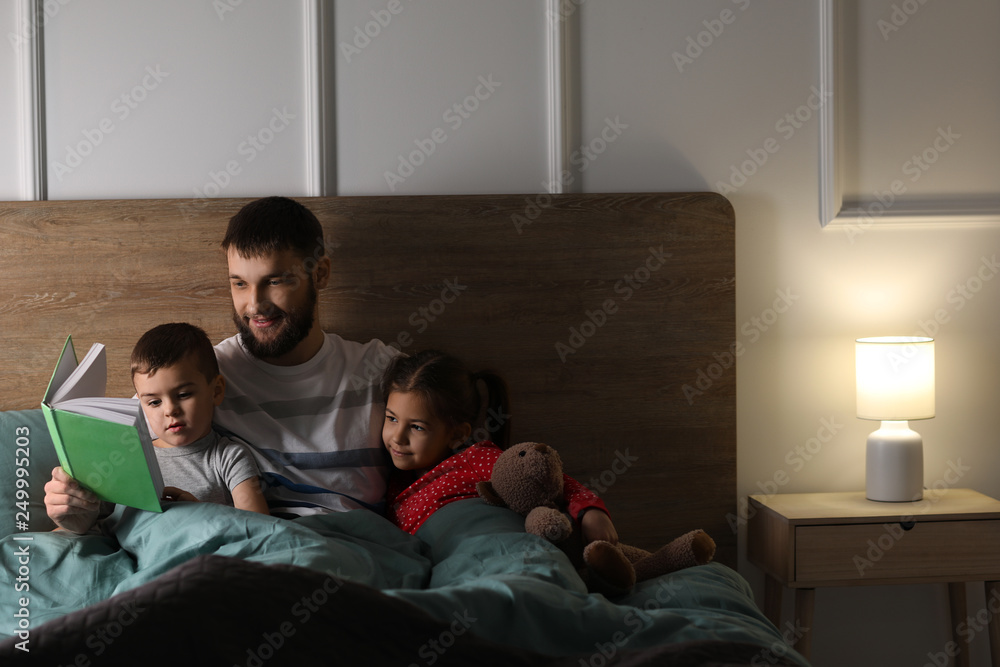 Young father reading book for his children in bed