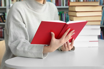 Canvas Print - Young woman reading books at table in library