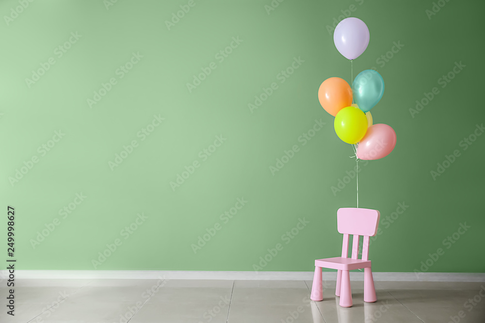 Small chair with balloons near color wall