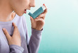 Young woman using inhaler against asthma on color background