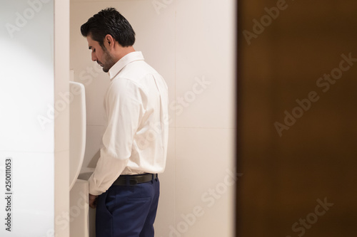 Fotografía Asian man urinating in toilet; portrait of Indian man using water closet, WC for