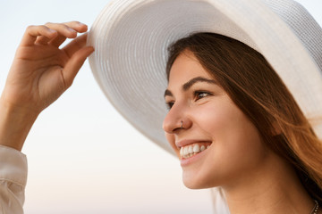 Wall Mural - Image of joyful woman 20s in summer straw hat smiling, while walking by seaside