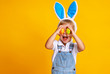 © JenkoAtaman - funny happy child boy with easter eggs and bunny ears on yellow.