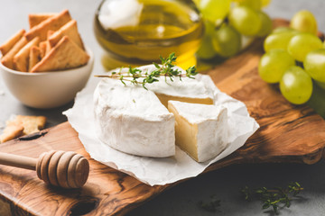 Brie or camembert cheese, crackers, honey, grapes on wooden serving board. Cheese board