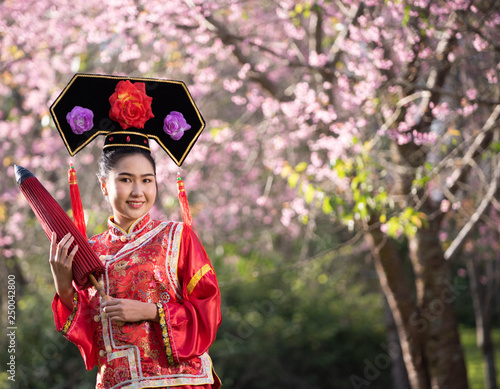 Plakat Beautiful Chinese young woman wearing red traditional cheongsam in cherry blossoms garden