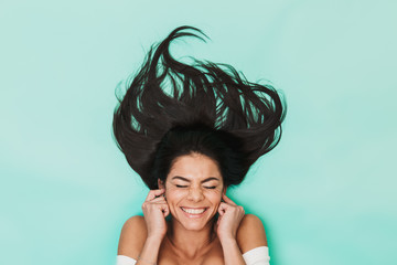 Wall Mural - Happy young woman lies isolated on blue light background covering ears.