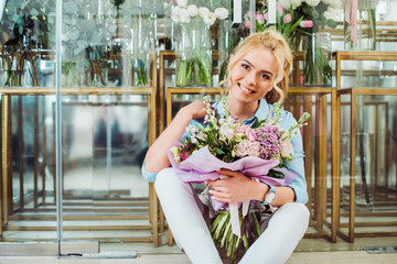 beautiful smiling woman holding flower bouquet while sitting in front of flower shop with copy space