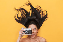 Happy Young Woman Lies Isolated On Yellow Background Holding Camera Photographing.
