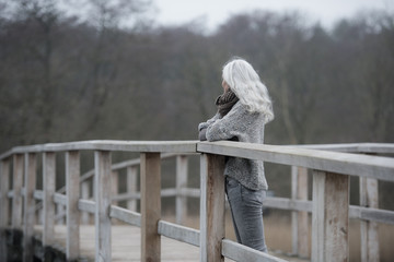 woman with long grey hair on a wooden bridge
