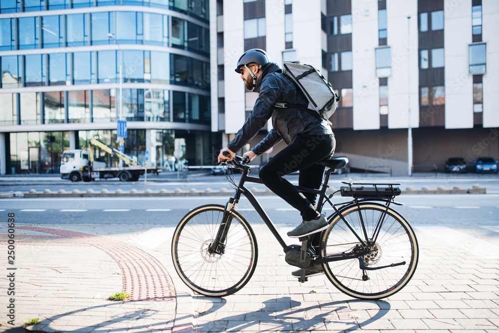 Male courier with bicycle delivering packages in city. Copy space. - obrazy, fototapety, plakaty 