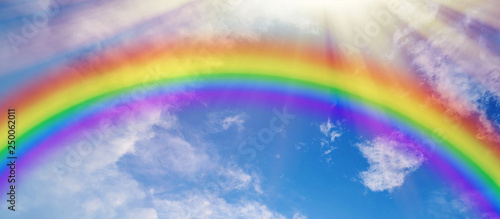 Colorful rainbow and sun rays on blue cloudy sky © Jürgen Fälchle