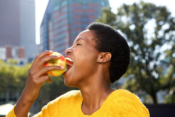 Wall Mural - side portrait of healthy young black woman eating apple outdoors