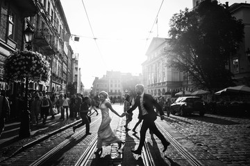 Wall Mural - elegant happy wedding couple running and laughing in sunlight in city streets at evening in european town. luxury bride and groom having fun. romantic sensual moment. black white photo