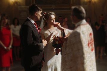 Beautiful bride and handsome groom kissing wedding rings, spiritual christian couple kissing gold rings during wedding ceremony in church, romantic moment