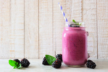 Blackberry Smoothie In A Mason Jar Glass With Scattered Berries Over A Rustic White Wood Background