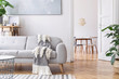 Modern scandianvian living room with design sofa with elegant blanket, coffee table and bookstand on the white wall. Brown wooden parquet. Concept of minimalistic interior. View on dining room.