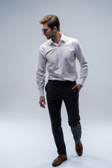 Wall Mural - young man in sunglasses looks to side while walking on gray studio background.
