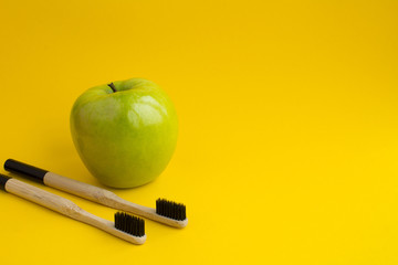 Two bamboo toothbrushes and green apple on the yellow background.Copy space.