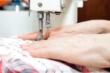 Sticker - Sewing on a sewing machine. Woman uses a sewing machine to sew clothes, decorations from material. Fashion and beauty concept, sewing clothes. A woman works at home, passion.