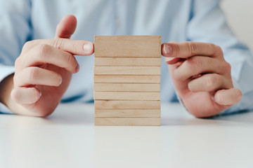 Wall Mural - Businessman in a blue shirt arranges wooden jigsaw blocks. The man arranges empty blocks one on top of the other. Different concepts to supplement with content. Business concept, HR.