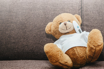 A small plush teddy bear measures a fever with an electronic thermometer. Medicine and health concept. Thermometer placed under the armpit of a teddy bear. Disease, flu and cold.