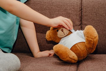 Wall Mural - A small plush teddy bear measures a fever with an electronic thermometer. Medicine and health concept. Thermometer placed under the armpit of a teddy bear. Disease, flu and cold.