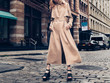 © Nick Starichenko - Fashionable woman wearing beige cotton long jacket and black high heels walking on city street of New York