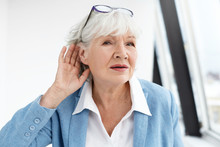 Come Again Please? Attractive Mature Woman Wearing Blue Jacket And Spectacles On Her Head Eavesdropping. Stylish Retired Female In Elegant Clothes Holding Hand At Her Ear, Suffering From Hearing Loss