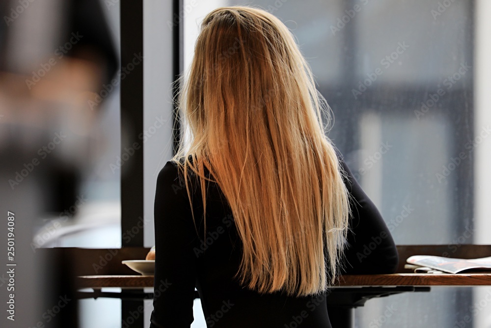 młoda kobieta blondynka siedzi tyłem w kawiarni miło spędza czas pije kawę czyta gazetę - obrazy, fototapety, plakaty 