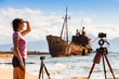 Woman with camera on tripod and shipwreck