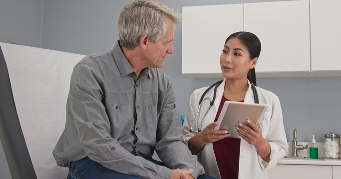 Wall Mural -  - Primary care doctor explaining medical issue to senior male patient in exam room. Female medical professional with tablet computer talking to older man about his health