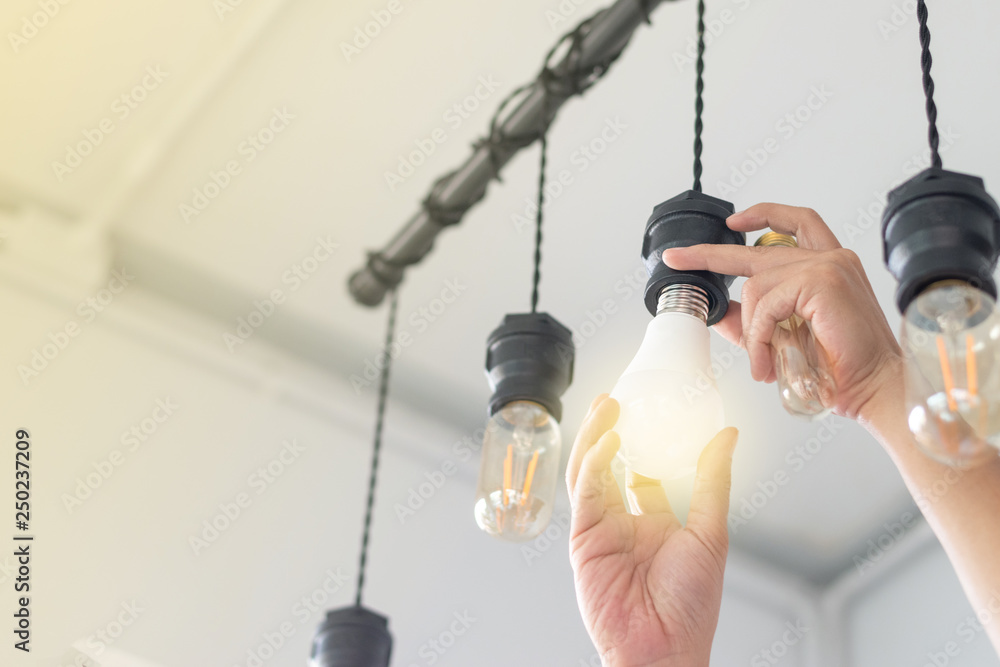 LED light Power saving concept. Asia man changing compact-fluorescent (CFL) bulbs with new  bulb. - obrazy, fototapety, plakaty 