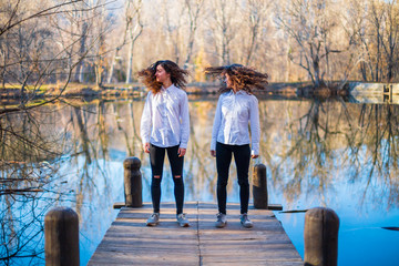 Young twin sisters in same clothes shaking hair at lake on autumn day in the forest