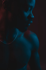 Wall Mural - Red and blue lighted portrait of young and sexy muscular shirtless man with neck chain. Flat shadows