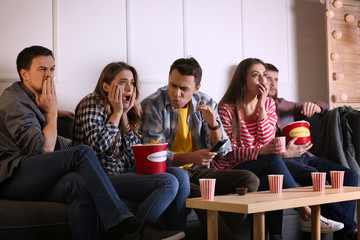 Canvas Print - Group of friends eating nuggets while watching horror movie on TV at home